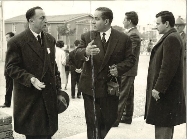 Δεκαετία τοῦ ‘60 - Οἱ ἐπίτροποι κ. Μαρκουλὴς καὶ κ. Ξυνὸς μπροστὰ στὸν ξύλινο Ναό. Τὸ Ε.Σ. εἶχε καθημερινὰ νὰ ἀντιμετωπίσει δύσκολα θέματα.